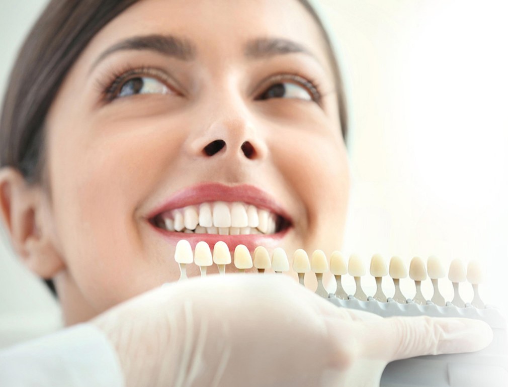 Tooth shade guide held against a patient's smile during teeth whitening at Smile 4U, Kurla